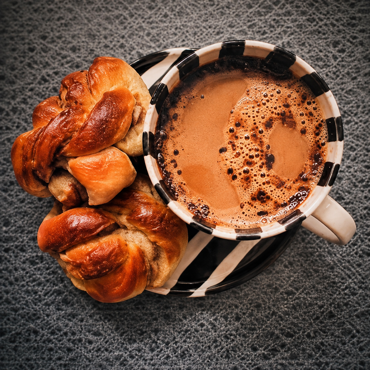 Kaffekopp och kanelbullar på randigt fat, sett uppifrån